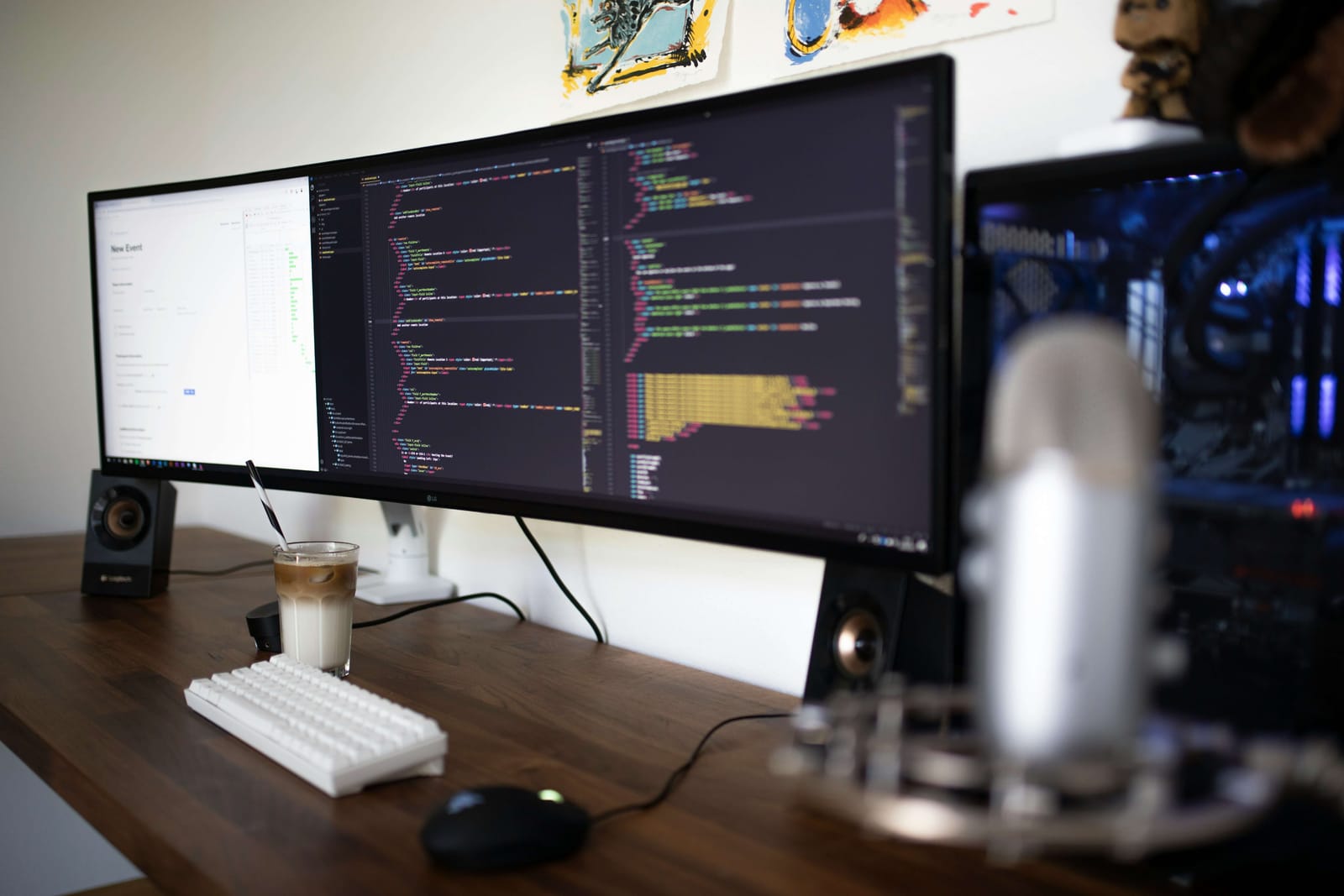 Widescreen monitor showing code on a desk with a keyboard and microphone