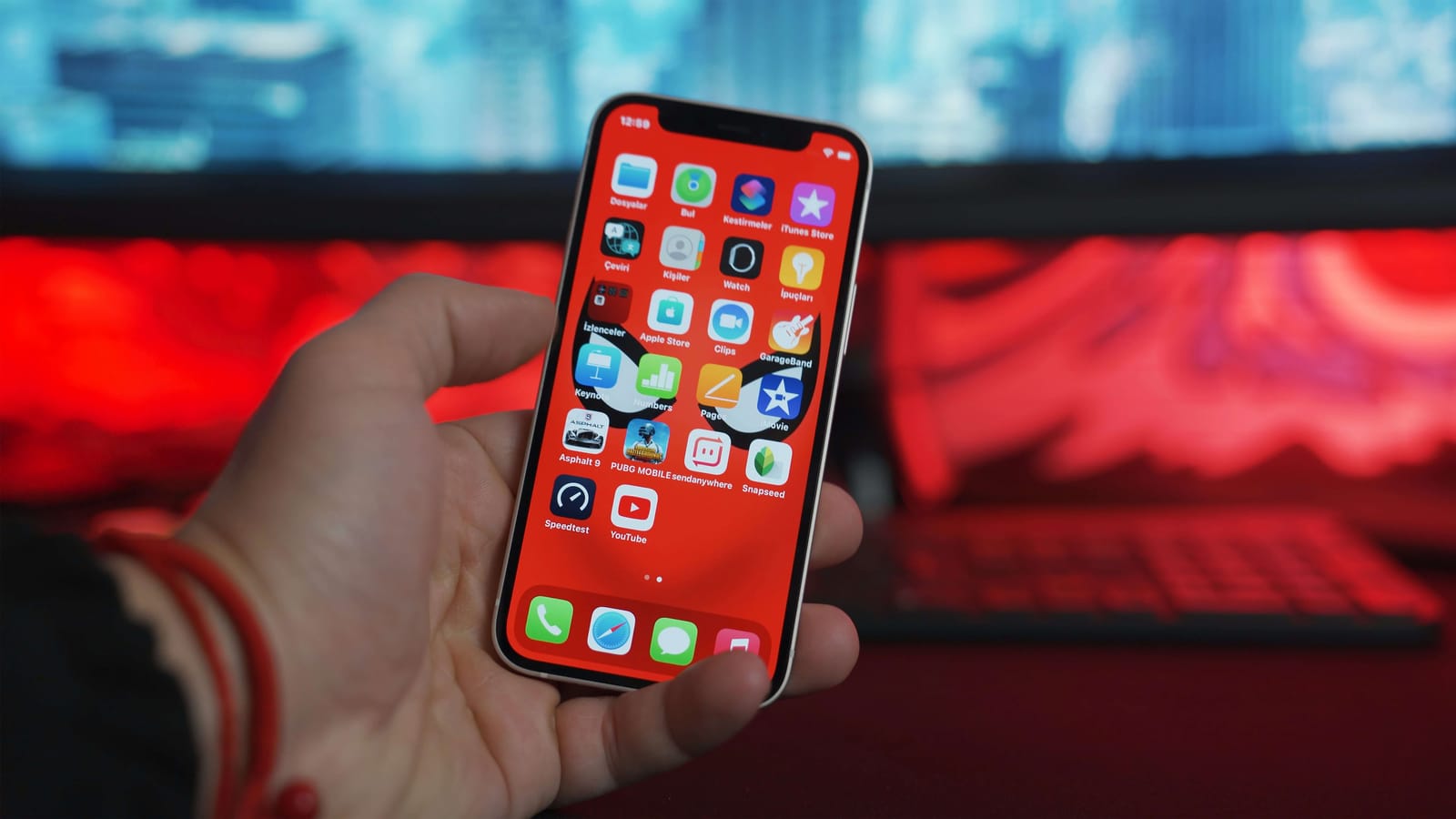 Hand holding an iPhone with a red home screen full of apps